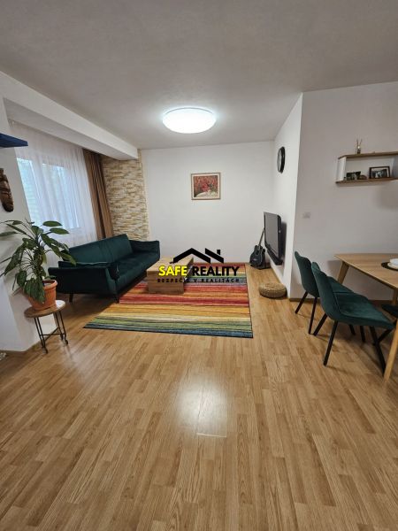 Obývací pokoj 3pokojového bytu s pestrým kobercem a podlahou s dřevěným dekorem.