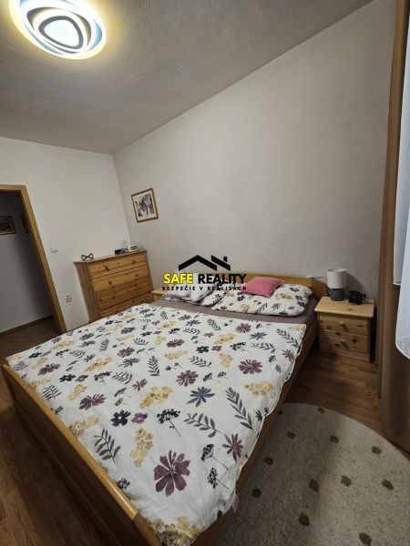 Ložnice v 3pokojovém bytě s postelí, komodou a podlahou s dřevěným dekorem.