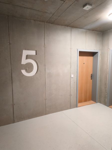 Betonová stěna s číslem pět a dřevěnými dveřmi v 2-pokojovém bytě.