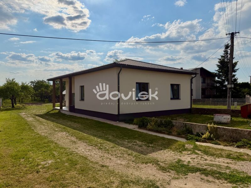 Rodinný dům v Zemplínské Široké obklopený zelení, jasná obloha nad střechou.