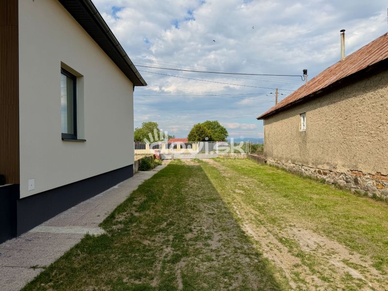 Rodinný dům v Zemplínské Široké s trávníkem mezi budovami a upraveným chodníkem.