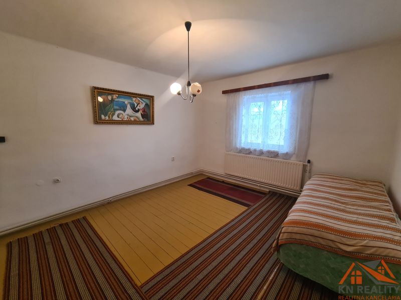 Interiér rodinného domu s postelí, obrazem a oknem se záclonami.