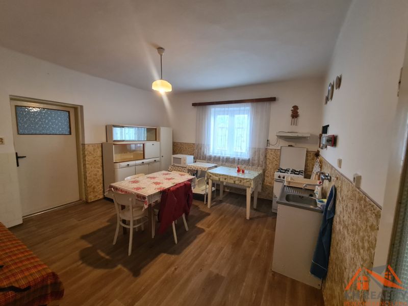 Kuchyně v rodinném domě s podlahou s dřevěným dekorem, jednoduchý nábytek a jídelní stůl.