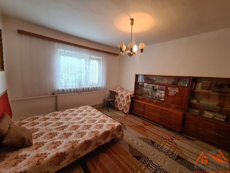 Pokoj s rozkládací pohovkou, starší vitrínou a závěsem, v rodinném domě.