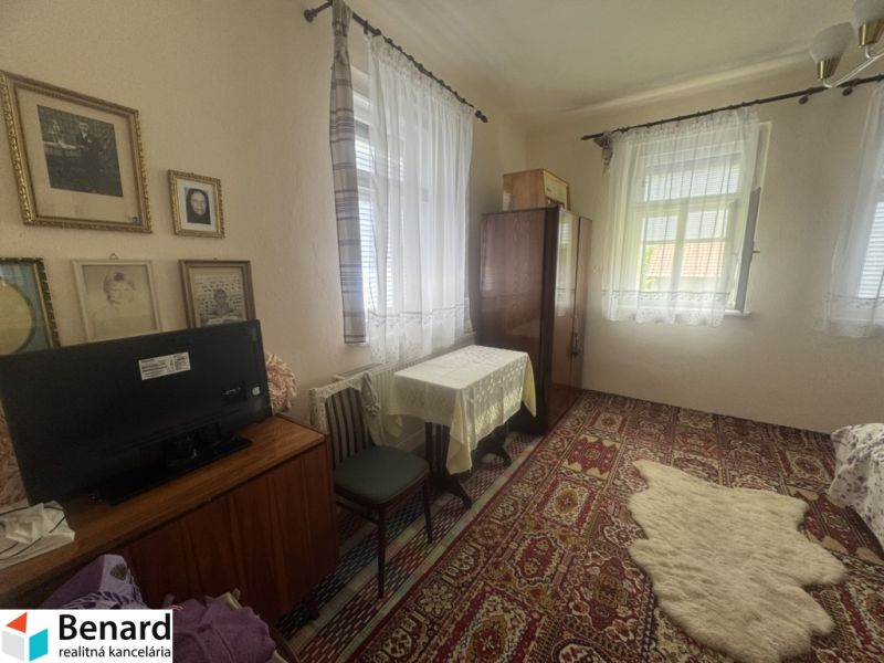 Pokoj s kobercem, stolem a televizí v rodinném domě. Vintage dekorace na stěnách.