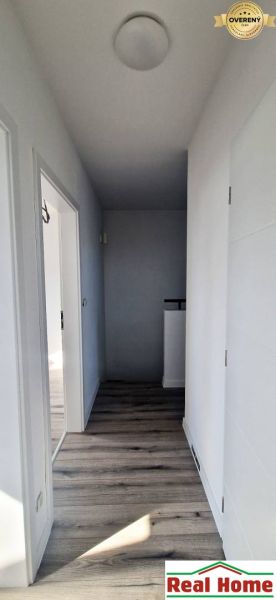 Chodba v rodinném domě s bílými stěnami a podlahou s dřevěným dekorem.