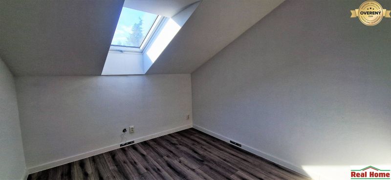 Podkrovní pokoj s velkým střešním oknem a podlahou s dřevěným dekorem v rodinném domě.