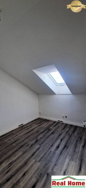 Podkrovní pokoj s podlahou s dřevěným dekorem a střešním oknem v rodinném domě.