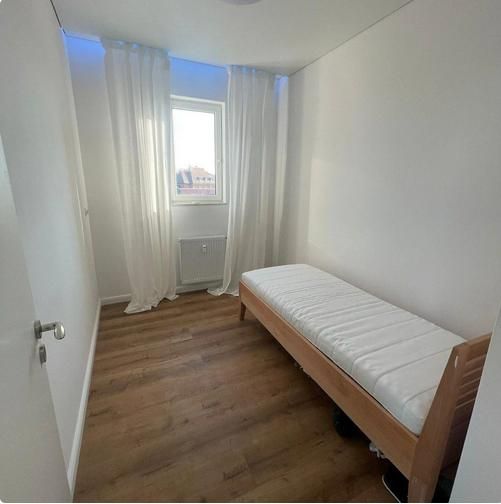 Úzký pokoj s postelí a podlahou s dřevěným dekorem ve 3pokojovém bytě.