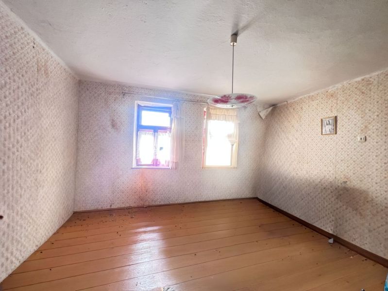 Prázdný pokoj v rodinném domě s podlahou s dřevěným dekorem a květinovým lustrem.