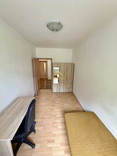 Pokoj ve 4pokojovém bytě s psacím stolem, skříní a podlahou s dřevěným dekorem.