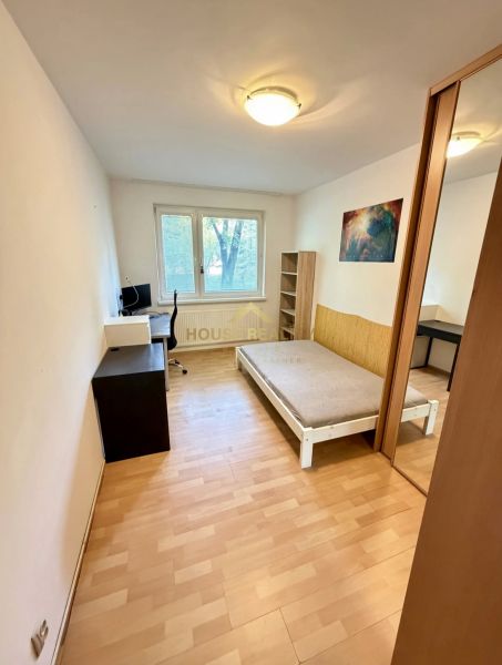 Pokoj ve 4pokojovém bytě s postelí, pracovním stolem a podlahou s dřevěným dekorem.
