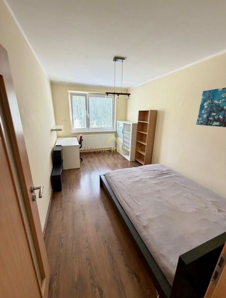 Ložnice ve 4pokojovém bytě s postelí, stolem a podlahou s dřevěným dekorem.