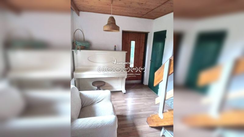 Interiér rodinného domu s bílým klavírem, podlaha s dřevěným dekorem, schody a dřevěný strop.