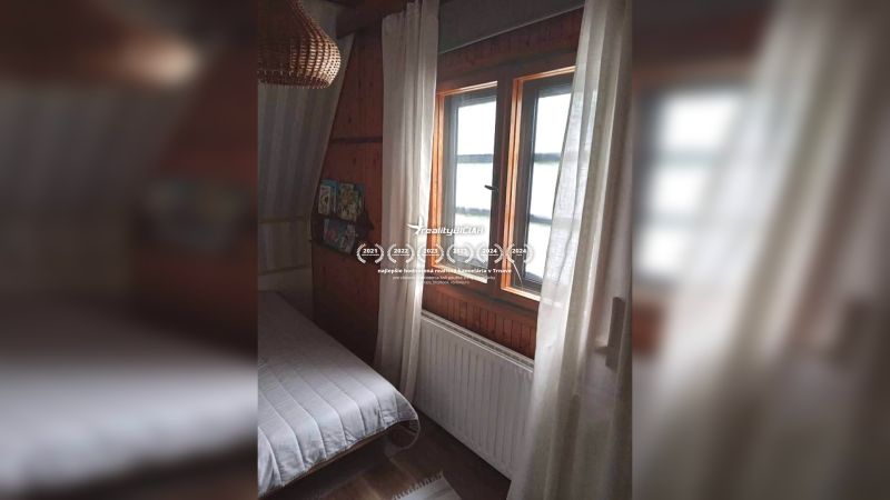 Pokoj v rodinném domě s tmavým dřevěným obkladem a postelí u okna.