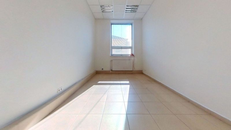 Světlá kancelář s dlaždicovou podlahou a velkým oknem propouštějícím světlo.