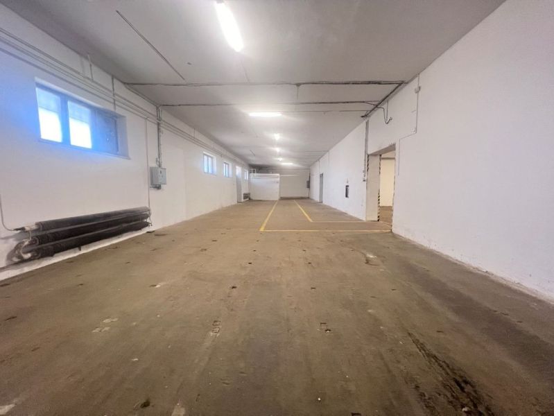 Interiér skladu s betonovou podlahou a bílými stěnami, zářivkové osvětlení.