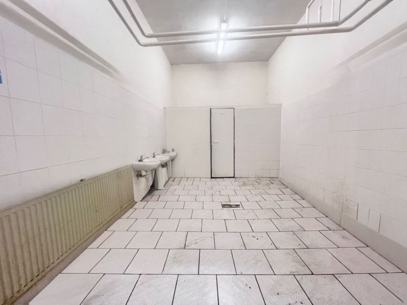 Interiér skladů a hal s bílými stěnami, dvěma umyvadly a dlaždicovou podlahou.