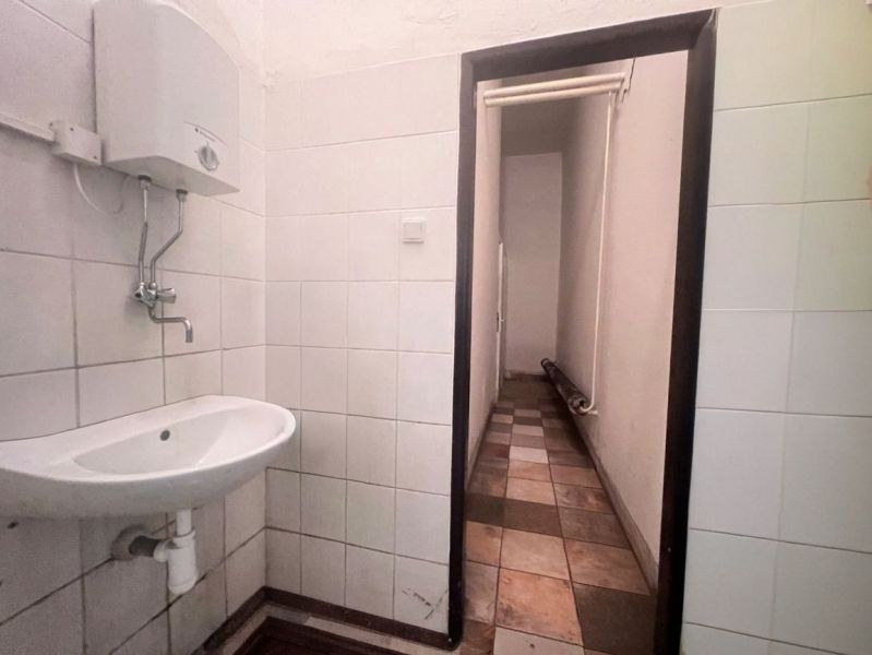 Interiér koupelny ve skladech a halách s umyvadlem a nástěnným ohřívačem vody.