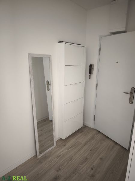 Vstupní chodba s bílým nábytkem a podlahou s dřevěným dekorem v 2-pokojovém bytě.