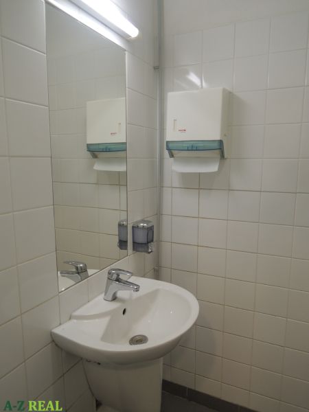 Umyvadlo v kancelářích s dávkovačem mýdla a zrcadlem na stěně.