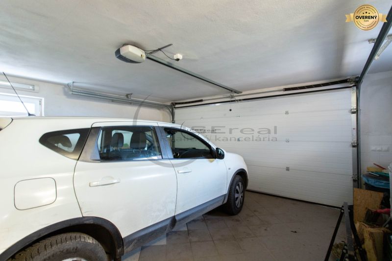 Auto zaparkované v garáži rodinného domu s bílými stěnami a podlahou z dlaždic.