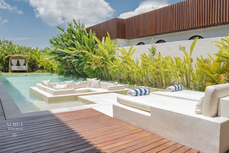 Luxusní vila na Bali s bazénem obklopeným zelení a relaxační zónou.