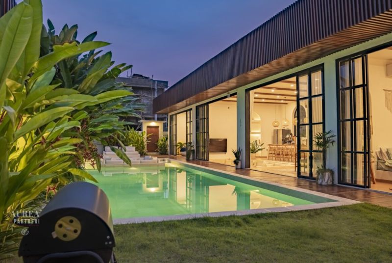 Vila na Bali s osvětleným bazénem, terasou s dřevěným dekorem a zahradou.
