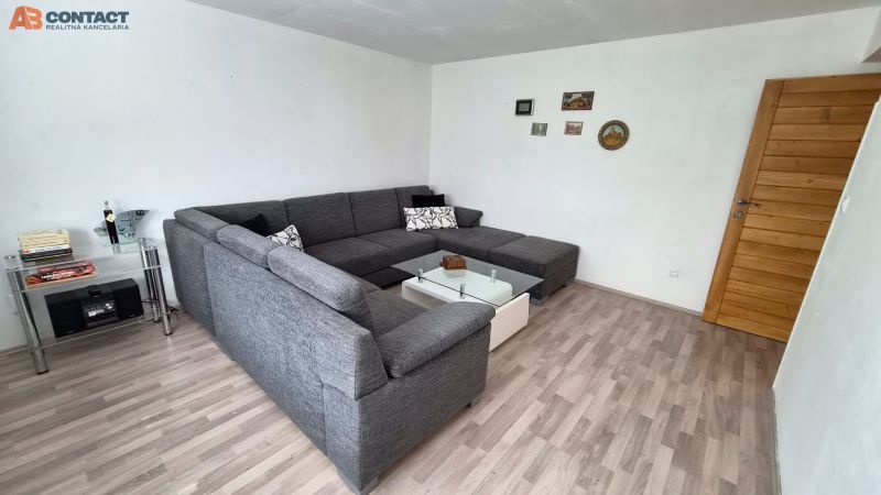 Obývací pokoj s rohovou sedačkou, skleněným stolkem a podlahou s dřevěným dekorem.