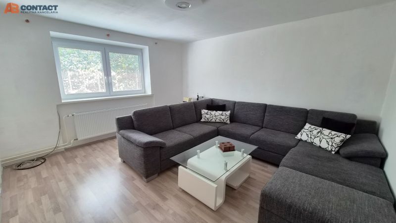 Obývací pokoj s rohovou šedou pohovkou a stolkem, podlaha s dřevěným dekorem.