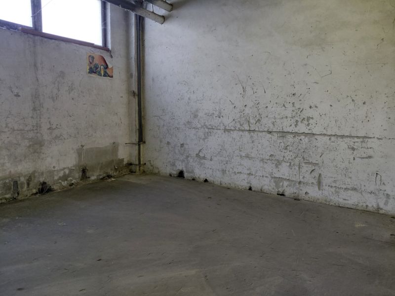 Průmyslový interiér s opotřebovanými stěnami a šedou podlahou, sklady a haly.