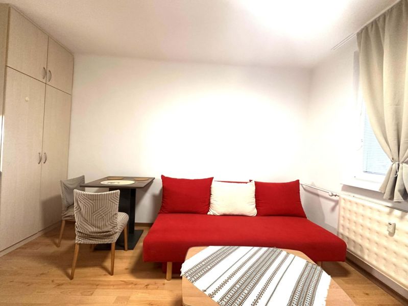Pokoj v rekreačním apartmánu s červenou pohovkou, stolem a podlahou s dřevěným dekorem.