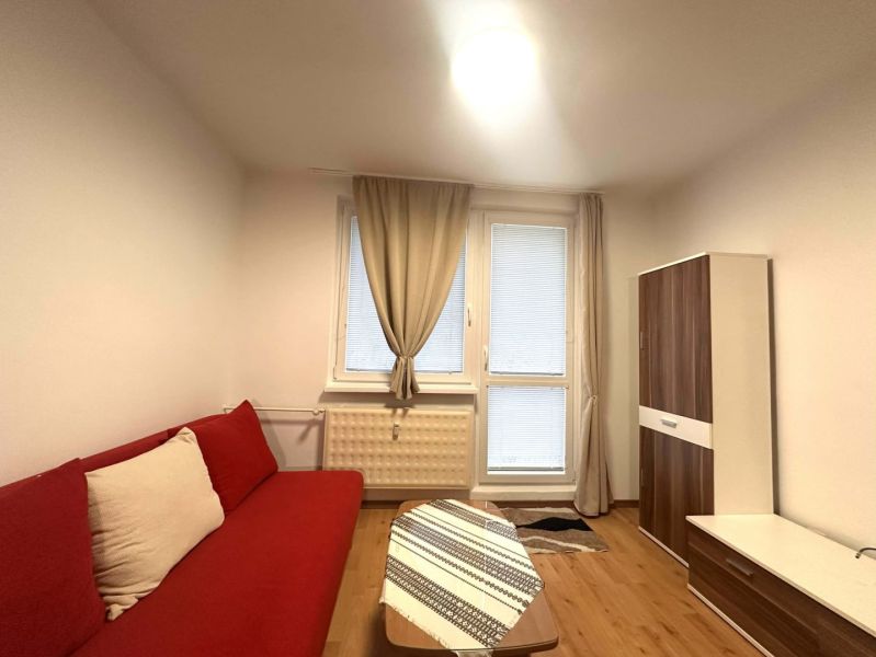 Rekreační apartmán s červenou sedačkou, dřevěným dekorem podlahy a skříní s dekorem dřeva.