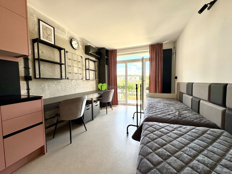 Garsonka s lůžky, pracovními stolky, moderním dekorem a výhledem na balkon.