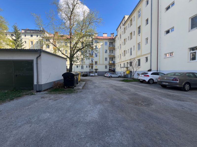 Parkoviště u bytového domu v Banské Bystrici s auty a stromy.
