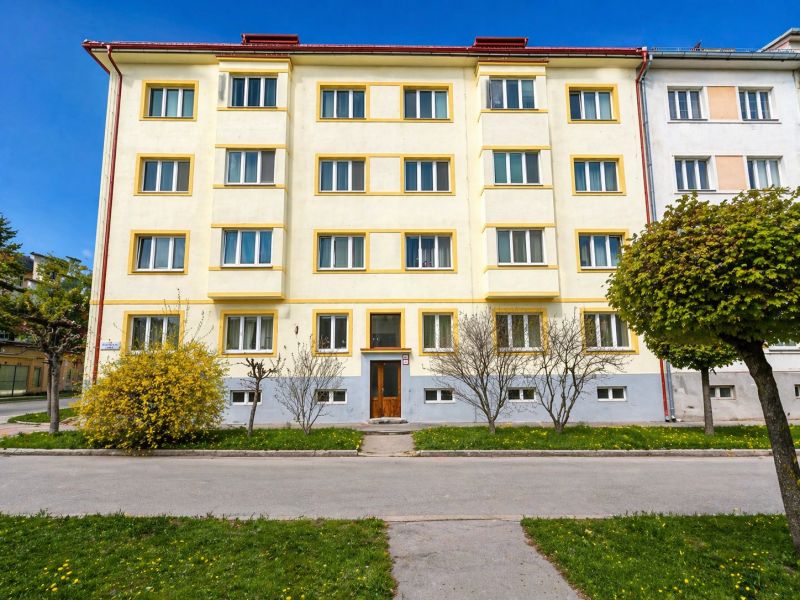 Bytový dům v Banské Bystrici, žlutá fasáda, upravená zeleň, jasná obloha.