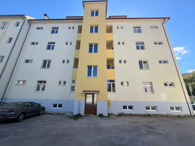 Bytovka v Banské Bystrici s parkovištěm před vchodem.