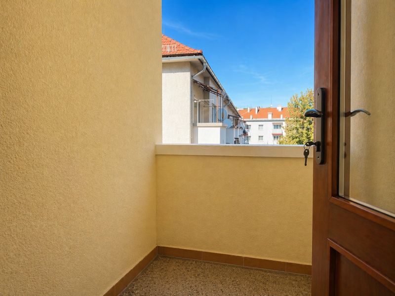 Balkon ve 4pokojovém bytě s výhledem na střechy a stromy.