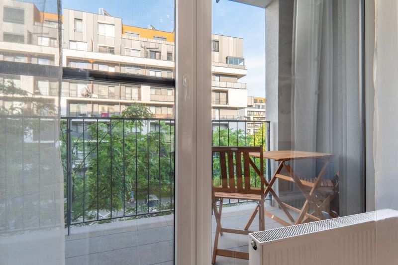 Výhled z 1-pokojového bytu na balkon se stolem a židlemi.