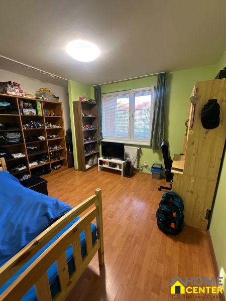 Pokoj v 3-pokojovém bytě s policemi, postelí a podlahou s dřevěným dekorem.