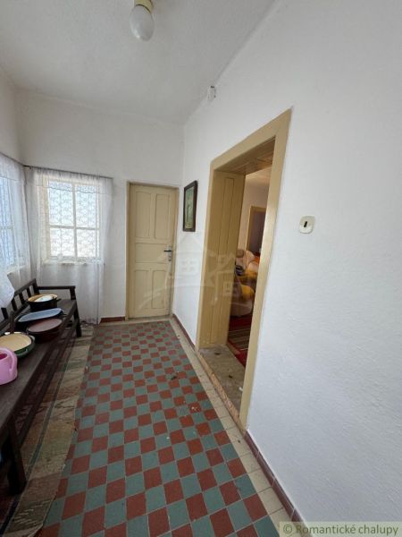 Chodba v rodinném domě s dlaždicovou podlahou, bílými stěnami a jednoduchým zařízením.