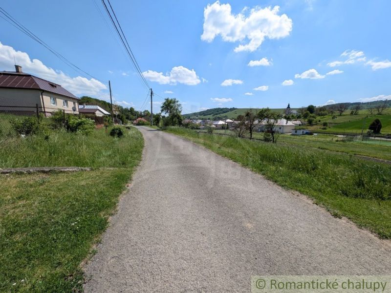 Cesta obklopená trávou vede přes venkovskou oblast v Karnej s výhledem na domy.