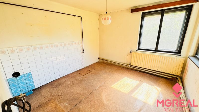 Nezařízená místnost s oknem, radiátorem a podlahou s dřevěným dekorem v rodinném domě.