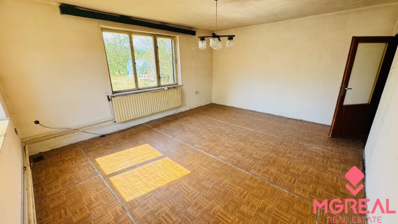 Pokoj s podlahou s dřevěným dekorem, velkým oknem a radiátorem v rodinném domě.