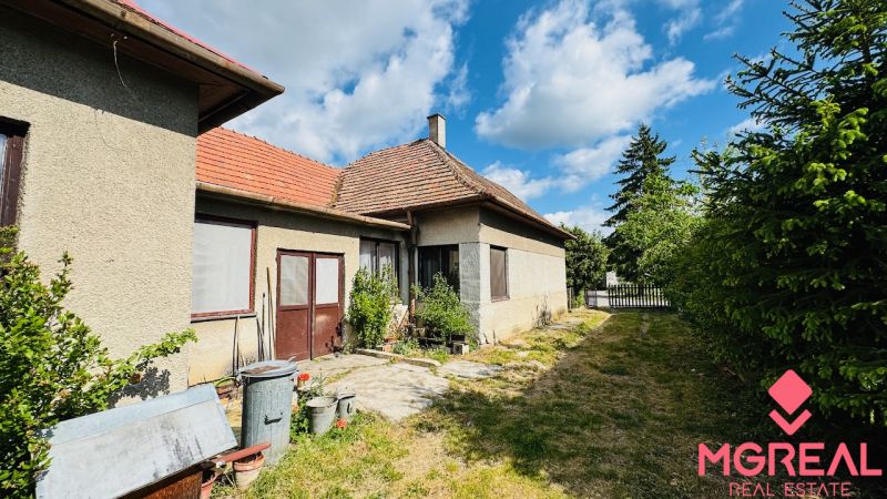 Rodinný dům v Pažiti se dvěma vchody, okna se sítěmi, vedle úzká zahrada.