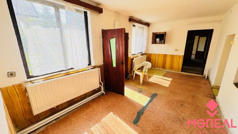 Interiér rodinného domu s otevřenými dveřmi, plastovými židlemi a velkými okny.