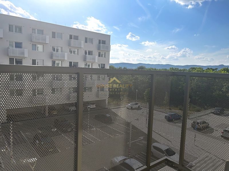 Balkon v 1-pokojovém bytě s výhledem na parkoviště a okolní hory.