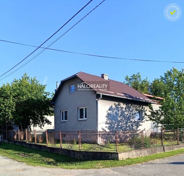Rodinný dům v Margecanech se šikmou střechou, oplocený, obklopený zelení a modrou oblohou.