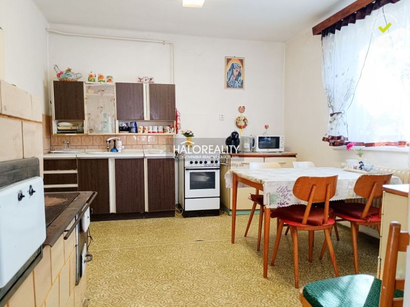 Kuchyně v rodinném domě se starším nábytkem, stolem a židlemi.