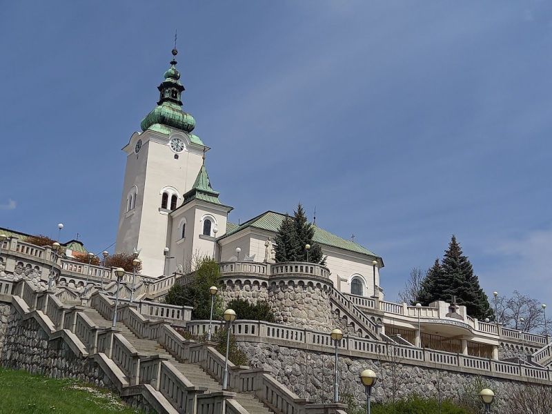 Kostel s věží obklopený schodištěm a zelení v Ružomberku.